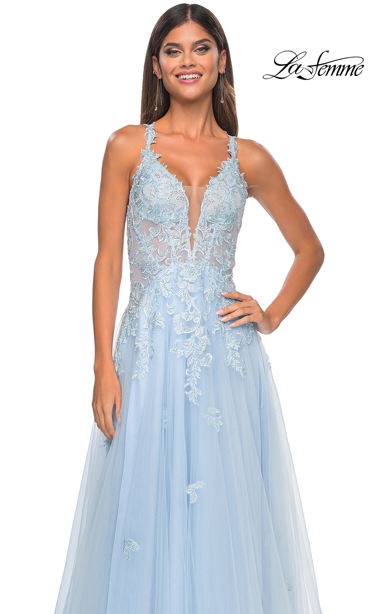 A woman in the Sheer-Waist Long A-Line Prom Dress (La Femme 32438) with light blue embroidered lace, a sheer bodice, and tulle skirt stands smiling. The sleeveless gown is elegant, with the La Femme logo in the top right corner.